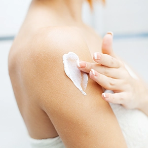 Una chica poniéndose crema en el cuerpo.