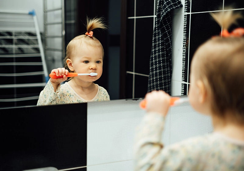 Una niña pequeña cepillándose los dientes frente al espejo.